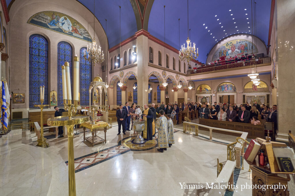 Greek Orthodox baptism ceremony inside an ornate church with clergy and congregation.
