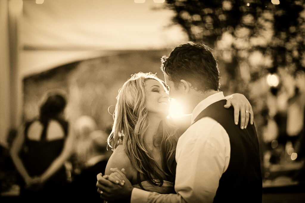 Bride and groom kiss on the dance floor with sunlight between them.