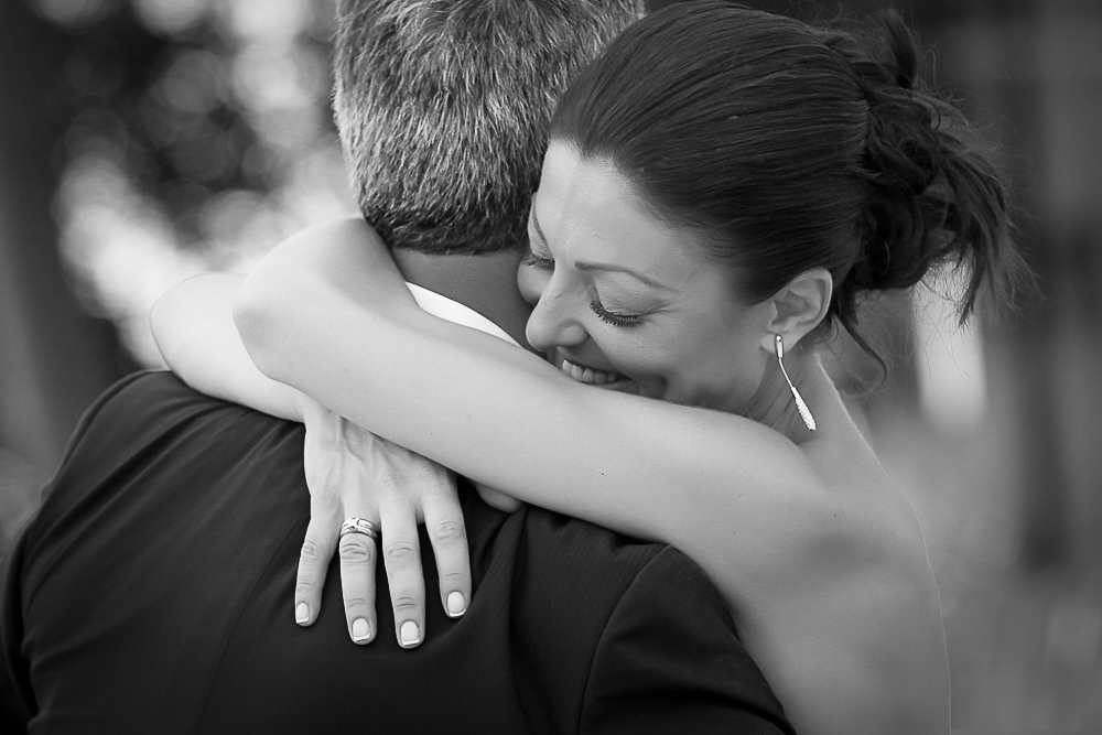 Smiling bride embraces her groom, with her wedding ring visible.