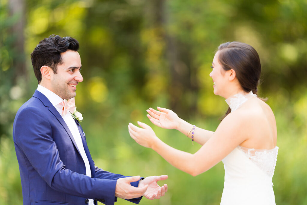 Bride and groom smile as they reach toward each other outdoors.