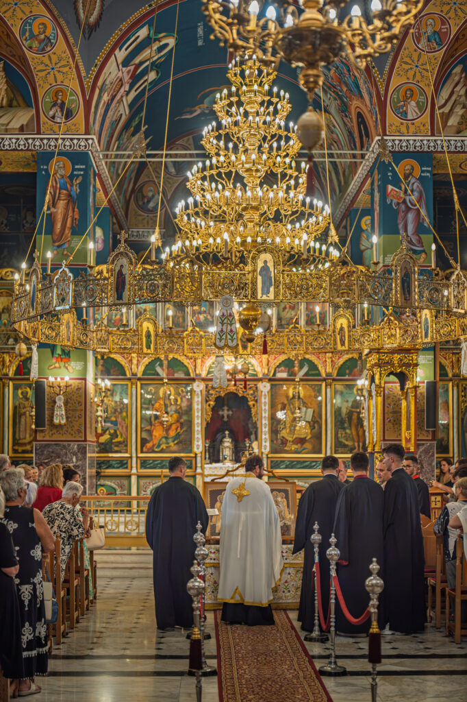 Clergy and worshippers gather beneath the chandeliers and iconostasis.